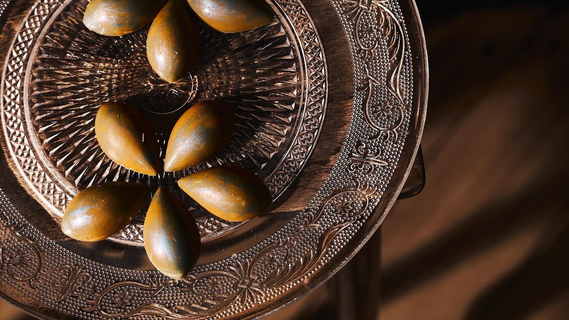 Ein dekoratives Tablett mit einer kunstvollen Metallstruktur. Darauf liegen mehrere braune, ovale Objekte.