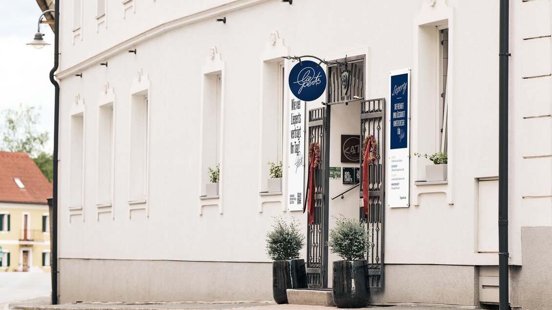 Ein einladendes Geschäft an einer Ecke mit einer weißen Fassade. Vor dem Eingang stehen dekorative Pflanzen in Töpfen.