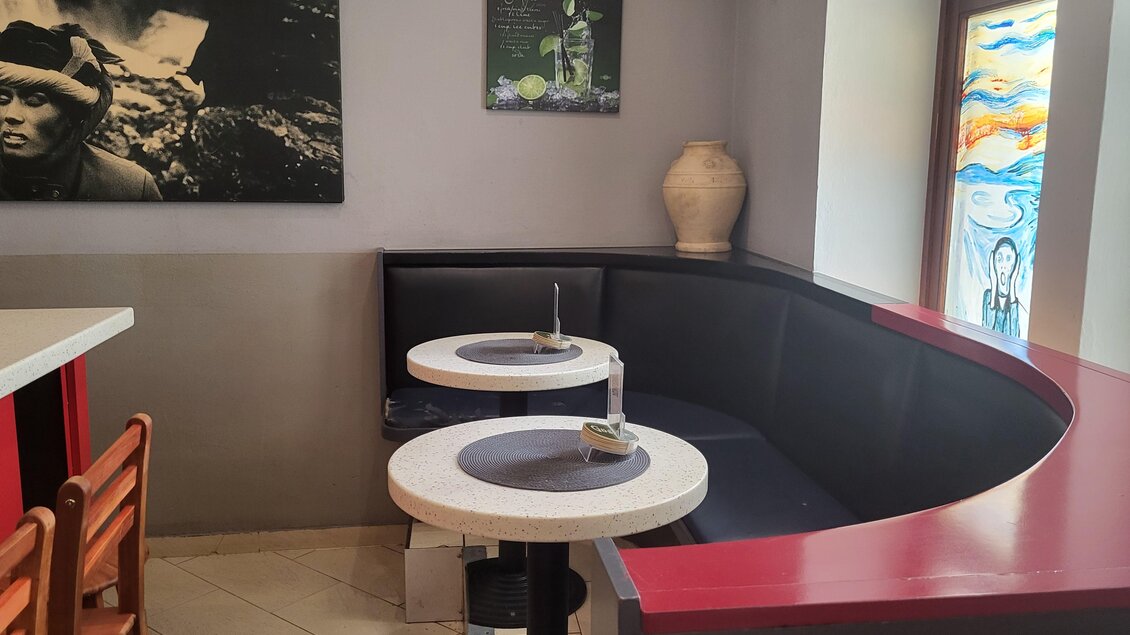 Ein gemütlicher Restaurantbereich mit einer halbkreisförmigen Sitzecke. An der Wand hängen Bilder und es gibt bunte Fensterdekoration. | © TV Hochsteiermark