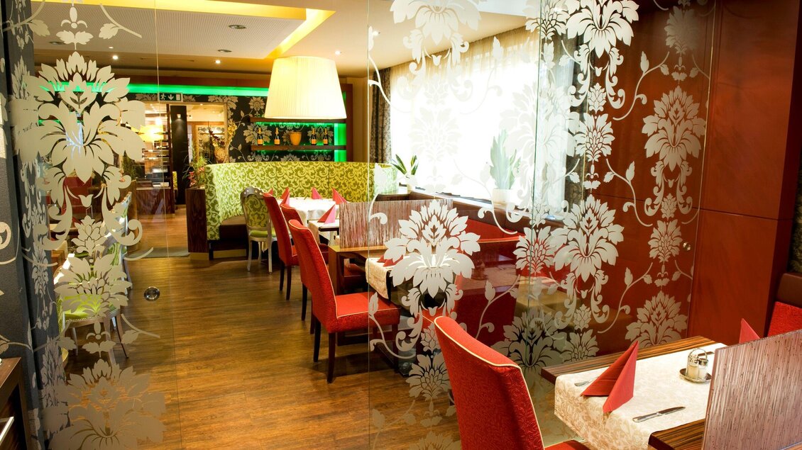 Ein elegantes Restaurant mit Holzfußboden und stilvollem Interieur. Rote Stühle und dekorative Glaswände schaffen eine einladende Atmosphäre. | © Lindenwirt - RP photography +