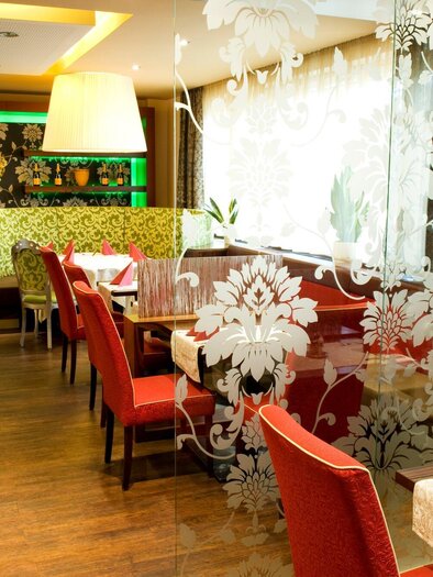 An elegant restaurant with wooden flooring and stylish interior. Red chairs and decorative glass walls create an inviting atmosphere. | © Lindenwirt - RP photography +