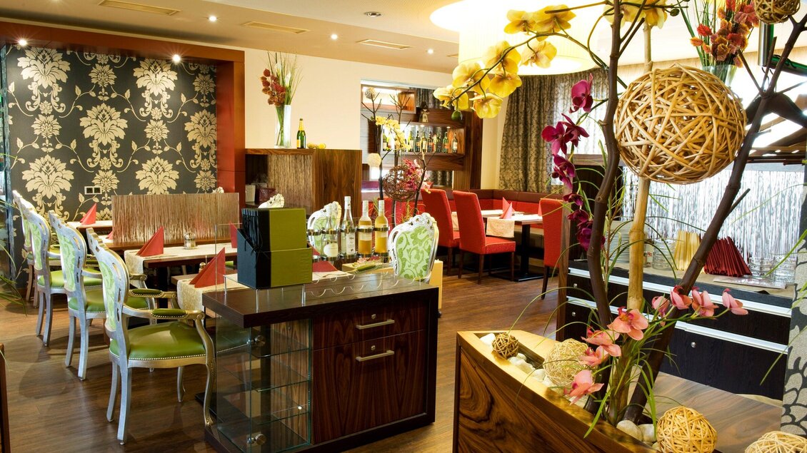 Ein stilvolles Restaurant mit bunten Stühlen und einem eleganten Dekor. Blumenarrangements und moderne Elemente verleihen dem Raum eine einladende Atmosphäre. | © Lindenwirt - RP photography +