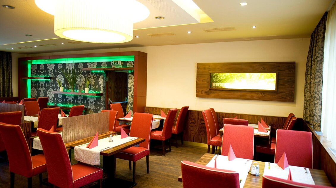 Ein elegantes Restaurant mit roten Stühlen und stilvollem Dekor. Die Tische sind gedeckt und die Beleuchtung sorgt für eine angenehme Atmosphäre. | © Lindenwirt - RP photography +