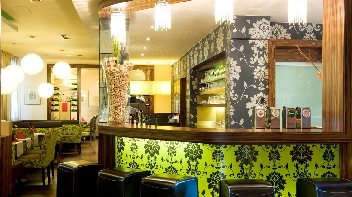 Ein modernes Restaurant mit stilvollem Dekor und einer eleganten Bar. Die Wände sind mit floralen Mustern in hellen Farben gestaltet. | © Lindenwirt - RP photography +