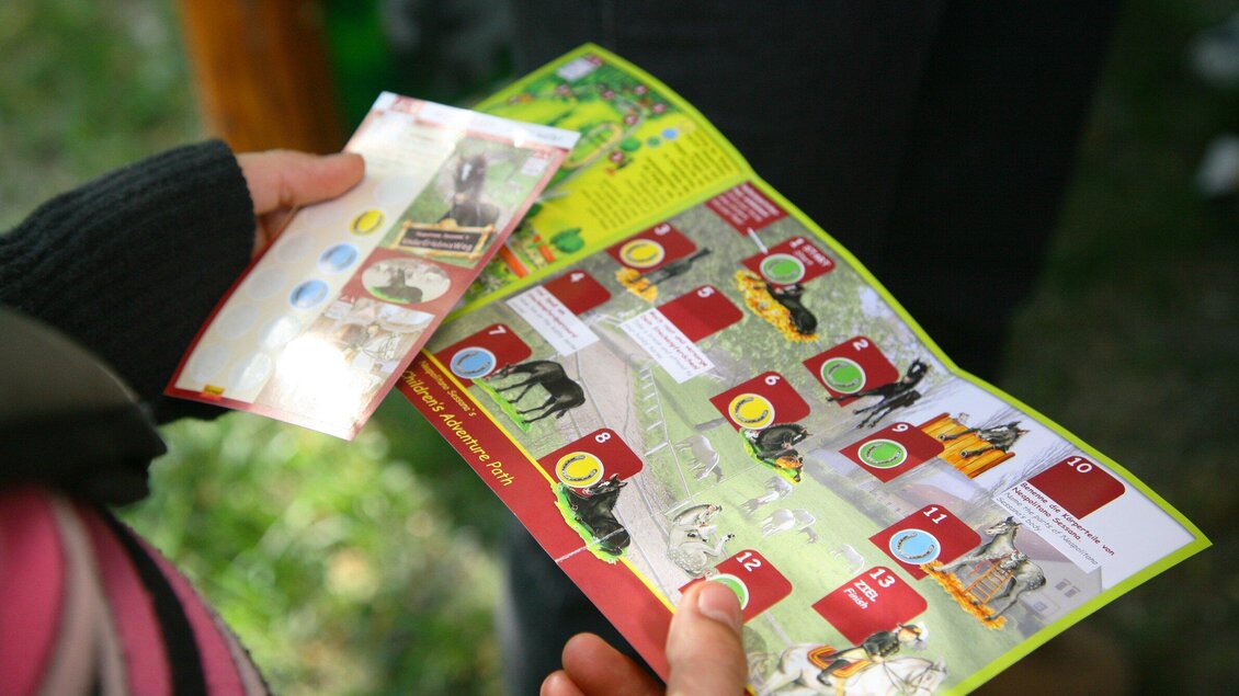 Eine Person hält eine bunte Karte in den Händen. Die Karte zeigt verschiedene Tiere mit Informationen und Bildern. | © SHS-LipizzanergestütPiberGöR