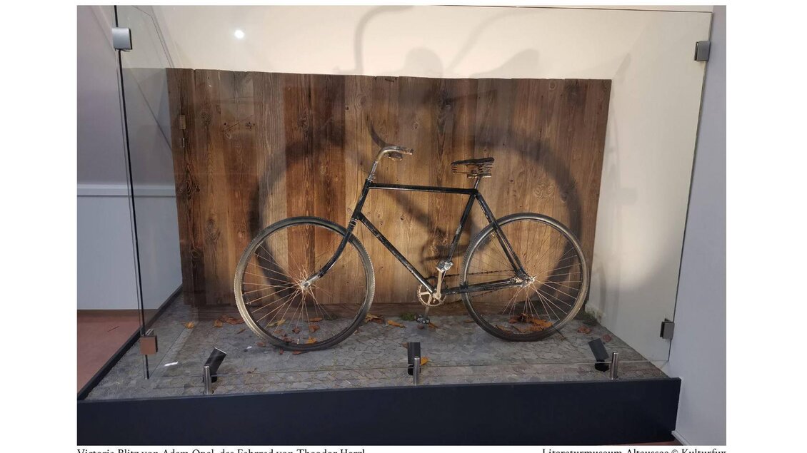 Ein antikes Fahrrad steht in einer Glasvitrine. Es ist ein "Victoria Blitz" von Adam Opel, umgeben von einer holzartigen Kulisse. | © Kulturfux