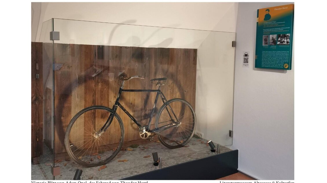Ein altes Fahrrad, das Victori Blitz von Adam Opel gehört, ist in einer Vitrine ausgestellt. Im Hintergrund ist eine hölzerne Wand zu sehen. | © Kulturfux