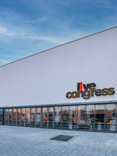 A modern conference building with large windows. The facade is simple and inviting, the colored text stands out from it. | © Foto Freisinger