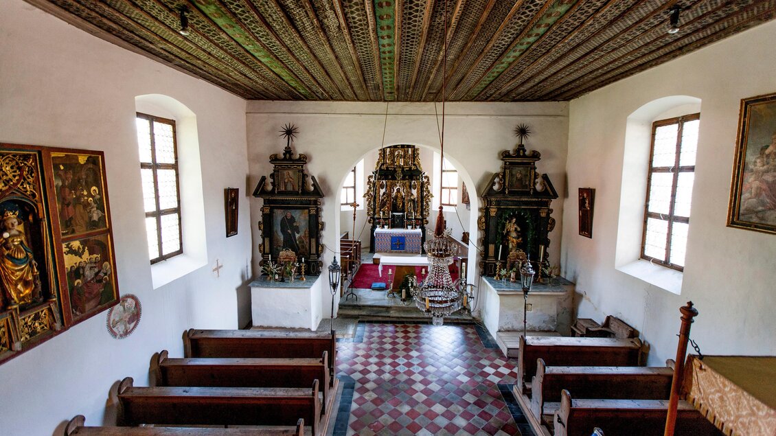 Eine kleine, historische Kirche mit einem kunstvoll gestalteten Altar. Die Bänke sind aus Holz und die Wände sind mit religiösen Bildern dekoriert. | © Holzwelt Murau