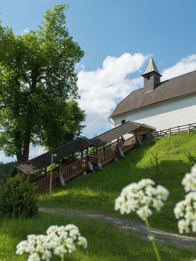 A small church stands on a hill, surrounded by trees and a green meadow. The sky is blue with a few clouds. | © Peter Wagner