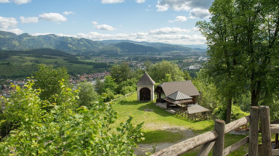 Eine malerische Landschaft mit Hügeln und Bäumen. Im Vordergrund steht ein kleines Häuschen und ein Zaun, mit Blick auf das Tal. | © Peter Wagner