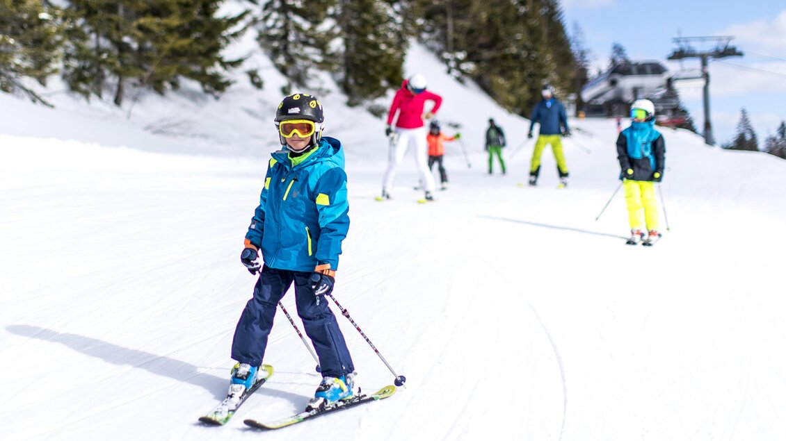 Ein Kind fährt Ski auf einer verschneiten Piste. Im Hintergrund sind weitere Skifahrer und Bäume zu sehen. | © TVB Ausseerland Salzkammergut_Tom Lamm
