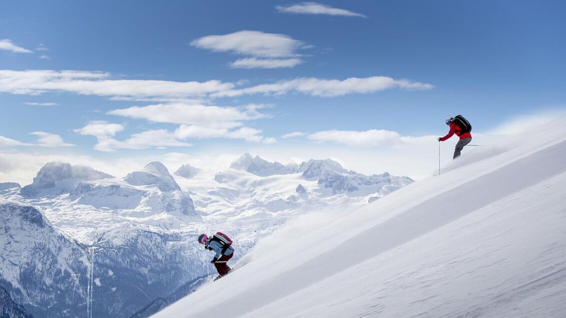 Zwei Skifahrer im Schnee mit beeindruckender Bergkulisse im Hintergrund. Der Himmel ist klar und blau, was perfekte Bedingungen für Wintersport bietet. | © TVB Ausseerland-Salzkammergut / Tom Lamm