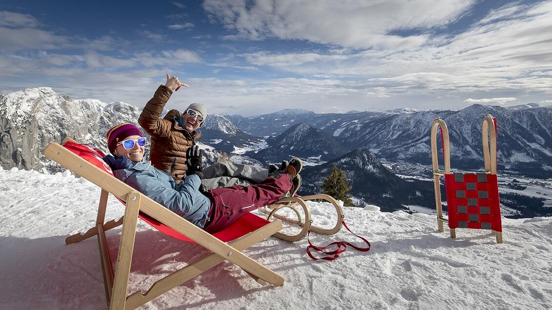 Zwei Personen entspannen auf einer Liege im Schnee und genießen die Aussicht auf die Berge. Im Hintergrund sind schneebedeckte Landschaften und ein klarer Himmel zu sehen. | © TVB Ausseerland-Salzkammergut / Tom Lamm
