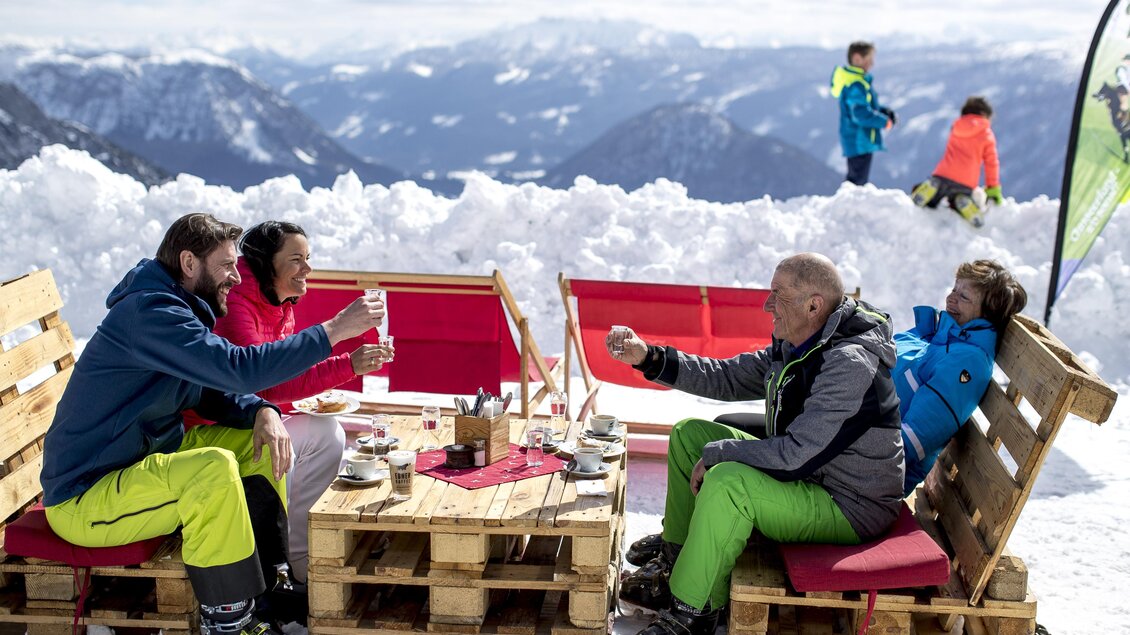 Eine Gruppe von Menschen sitzt in einer Lounge aus Paletten auf einem Berg. Umgeben von Schnee genießen sie die Aussicht und ihre Zeit zusammen. | © Ausseerland Salzkammergut / Tom Lamm