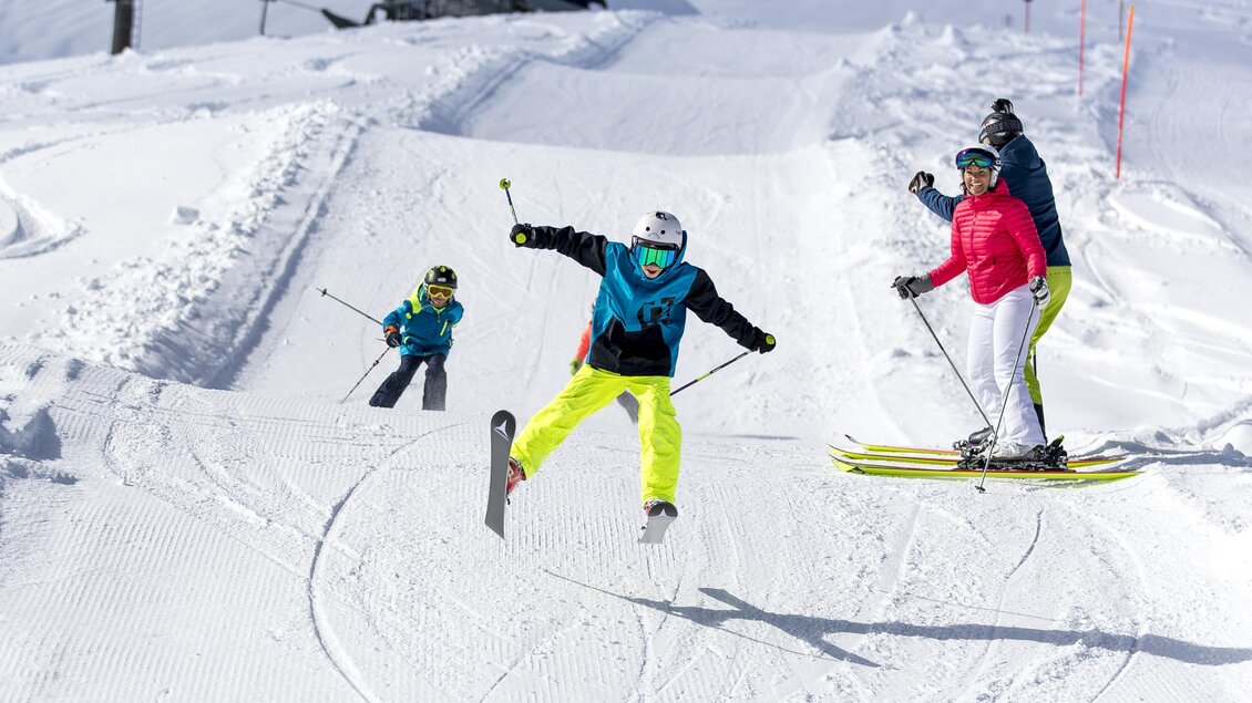 Eine Gruppe von Skifahrern auf einer verschneiten Piste. Ein Kind springt fröhlich über die Skispur. | © TVB Ausseerland - Salzkammergut / Tom Lamm