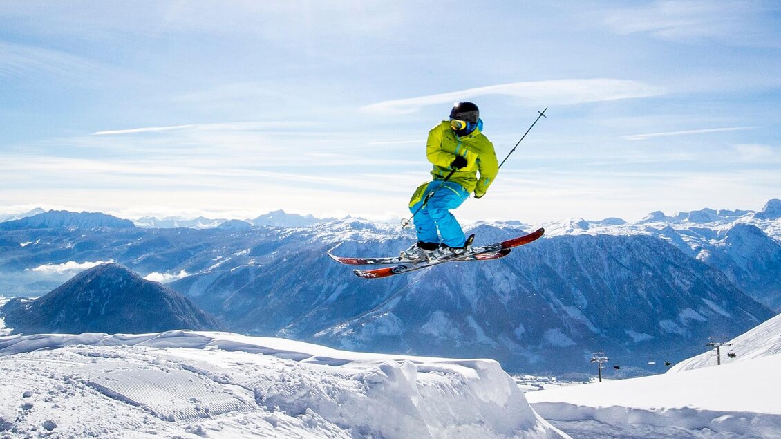 Ein Skifahrer springt in die Luft und zeigt einen beeindruckenden Trick. Die schneebedeckte Berglandschaft und der klare Himmel schaffen eine atemberaubende Kulisse. | © TVB Ausseerland - Salzkammergut / Tom Lamm