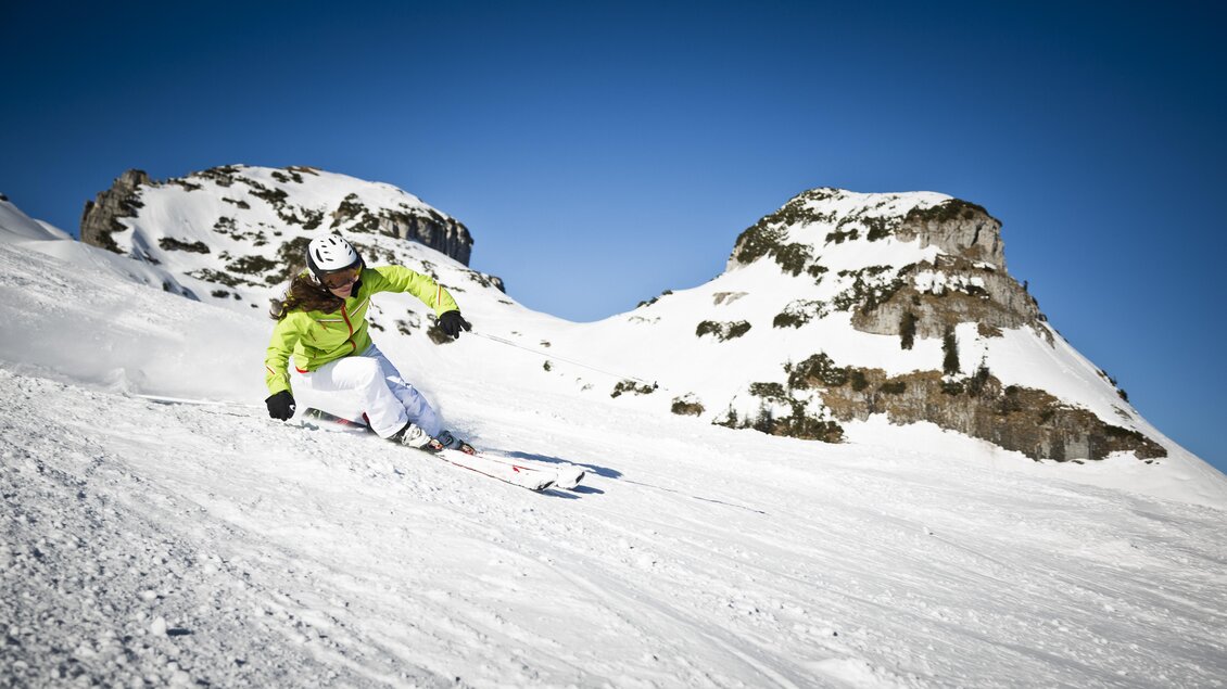 Ein Skifahrer fährt die Piste hinunter, umgeben von schneebedeckten Bergen. Der Himmel ist klar und blau. | © Loser Bergbahnen/mirjageh.com
