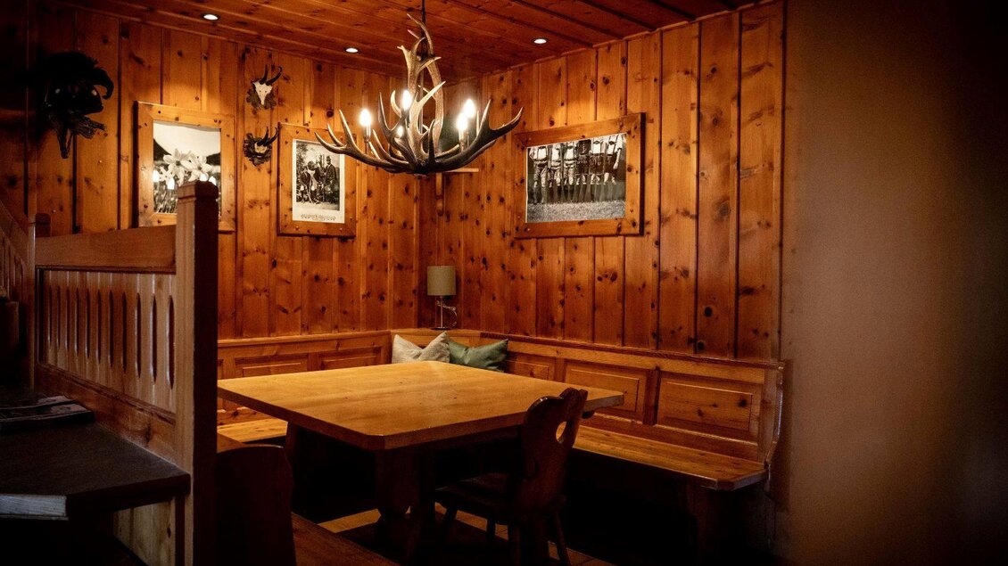 Ein gemütlicher Raum mit Holzwänden und einer langen Holzbank. Über einem großen Tisch hängt eine dekorative Antler-Leuchte. | © Chris Gütl