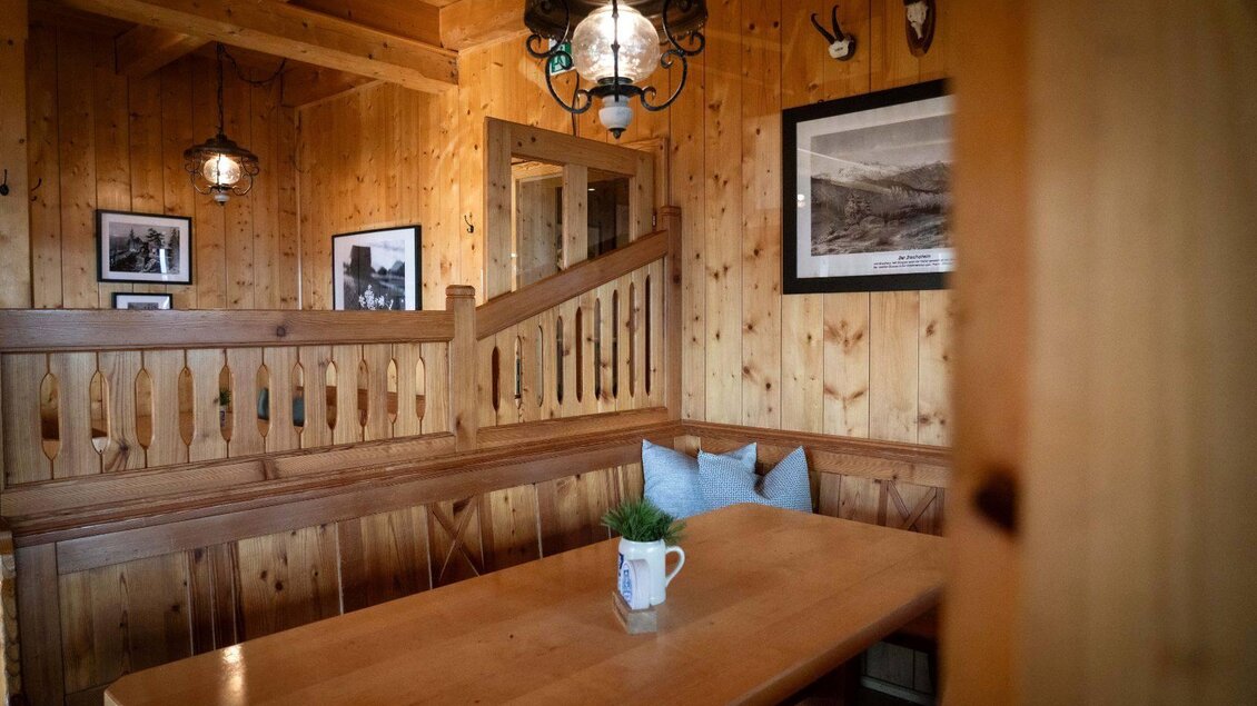 Ein gemütlicher Essbereich aus Holz mit einer langen Tafel und bequemen Sitzbänken. An den Wänden hängen schöne Bilder, und eine Pflanzen dekoriert den Tisch. | © Chris Gütl