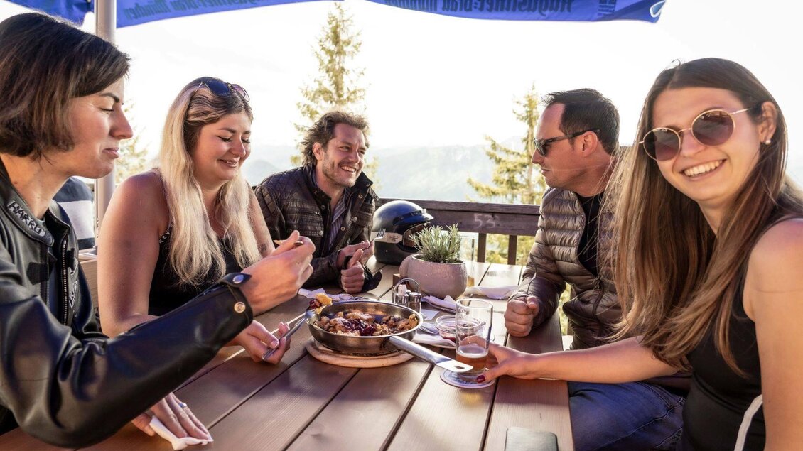 Eine Gruppe von fünf Personen sitzt an einem Tisch im Freien und genießt ein Essen. Die Umgebung ist sonnig und die Stimmung wirkt entspannt und freundlich. | ©  Chris Gütl