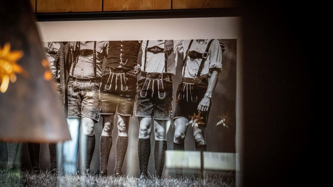Ein Schwarz-Weiß-Foto von mehreren Männern in traditionellen bayerischen Trachten. Sie stehen in einer Reihe mit kurzen Lederhosen und hohen Socken. | © Chris Gütl