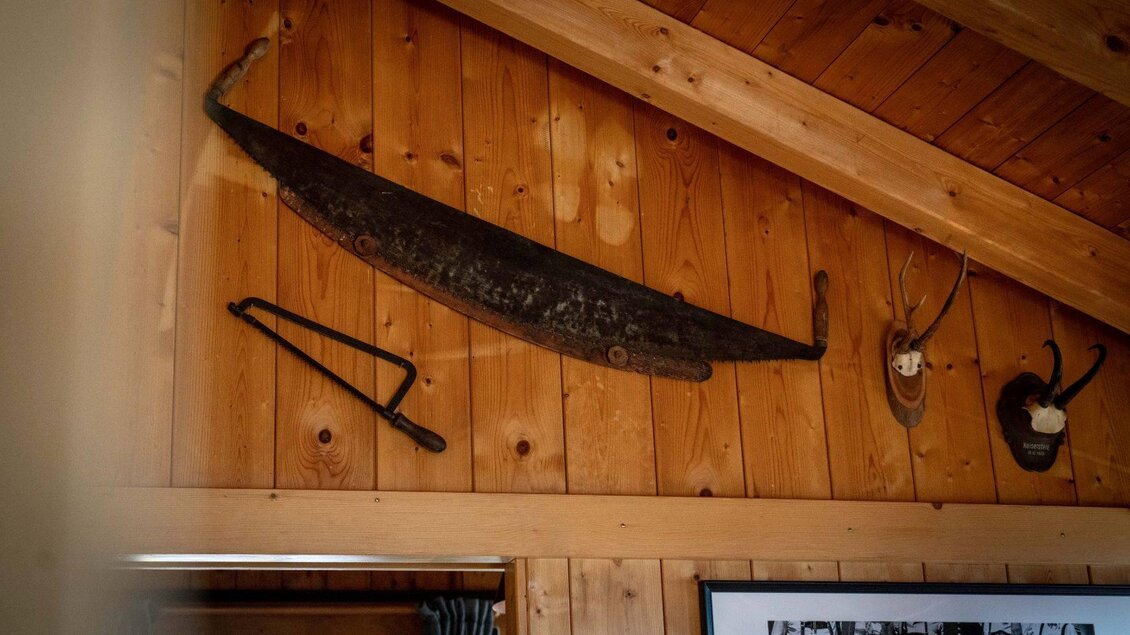 Eine rustikale Wand aus Holz mit verschiedenen alten Werkzeugen und Jagdtrophäen. Oben hängt ein nostalgisches Bootsteil. | ©  Chris Gütl