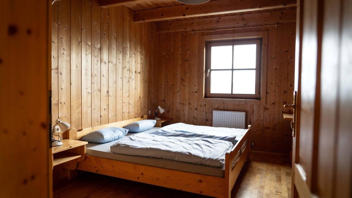 Ein gemütliches Schlafzimmer mit Holzvertäfelung. Das Doppelbett steht neben einem Fenster und einem Nachttisch. | ©  Chris Gütl