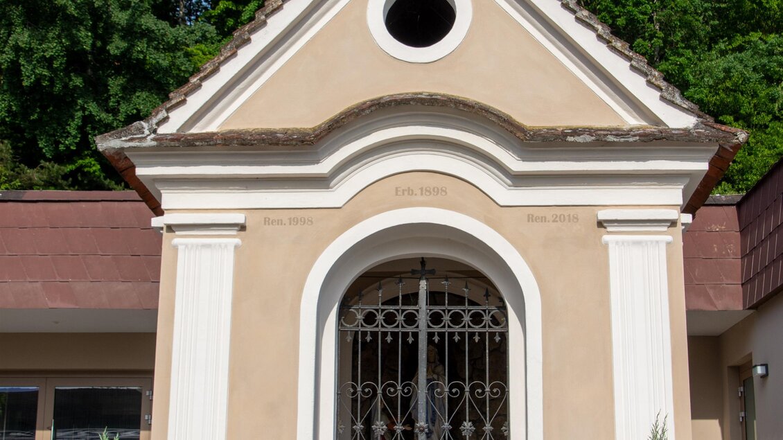 Eine kleine Kapelle mit einer schönen Fassade und einem runden Fenster. Umgeben von Bäumen und geschmackvoll gestaltetem Grün. | © Kurkommission Bad Blumau