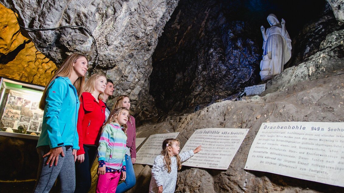 Eine Gruppe von Frauen und Mädchen steht in einer Höhle und betrachtet eine Statue. An den Wänden sind Informationsschilder angebracht. | © TV Region Graz - Mias Photoart