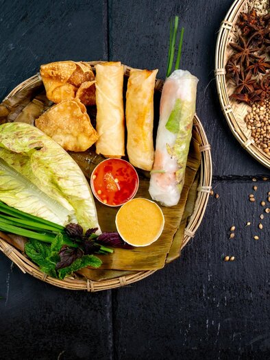 Spring rolls, wontons, rice paper rolls, leaf salad, herbs, and dips arranged on bamboo plates. | © Má Kitchen