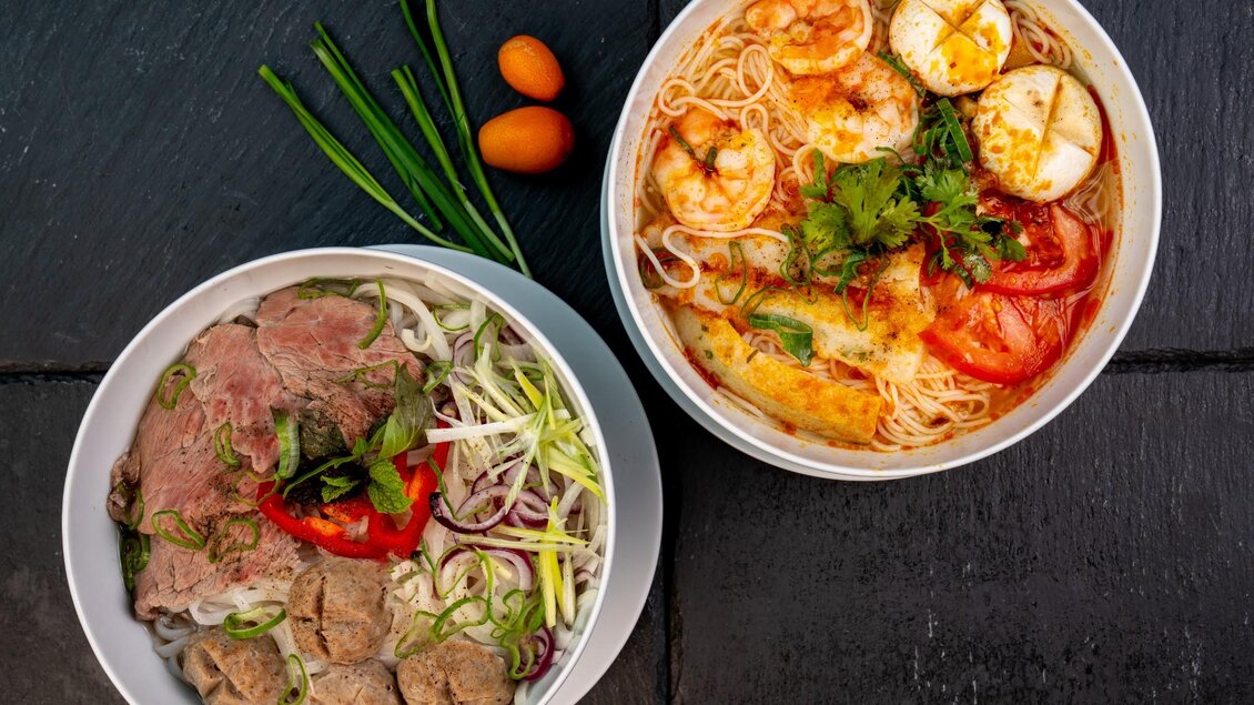 Zwei Schalen mit Pho Bo und Garnelen-Nudelsuppe, garniert mit Kräutern, Gemüse, Tofu und Ei . | © Má Kitchen