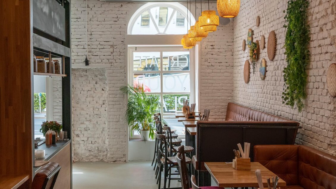 Innenraum mit weißen Ziegelwänden, Holzdeko, Korblampen und Sitznischen am Fenster. | © Má Kitchen