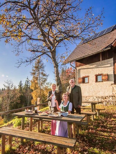 Eine Gruppe von Menschen steht vor einem gemütlichen Bauernhaus in einer malerischen Landschaft. Der Himmel ist klar und die Umgebung wirkt einladend und herbstlich. | © Stift Rein - Pater Martin