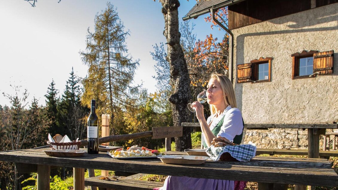 Frau in Tracht genießt Wein und Jause vor der Mühlbacher Hütte in der Steiermark | © Stift Rein - Pater Martin