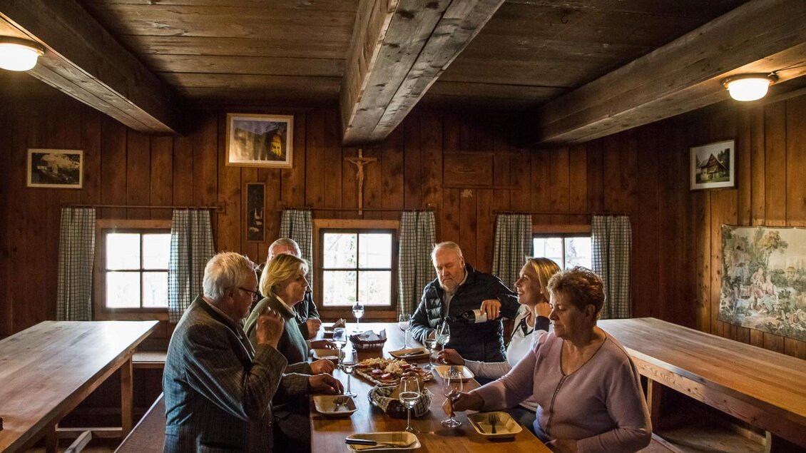 Eine gemütliche Stube mit einer Gruppe von sechs Personen, die zusammen essen und trinken. Die Einrichtung ist rustikal mit Holzwänden und warmem Licht. | © Stift Rein - Pater Martin