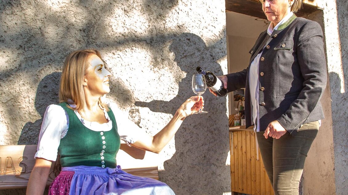 Zwei Frauen in traditioneller Kleidung genießen einen Moment zusammen. Eine Frau reicht der anderen ein Glas Wein. | © Stift Rein - Pater Martin