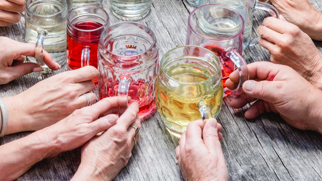 Eine Gruppe von Händen hält verschiedene Gläser mit Getränken. Der Tisch ist aus Holz und die Getränke sind bunt. | © TV Region Graz - Mias Photoart