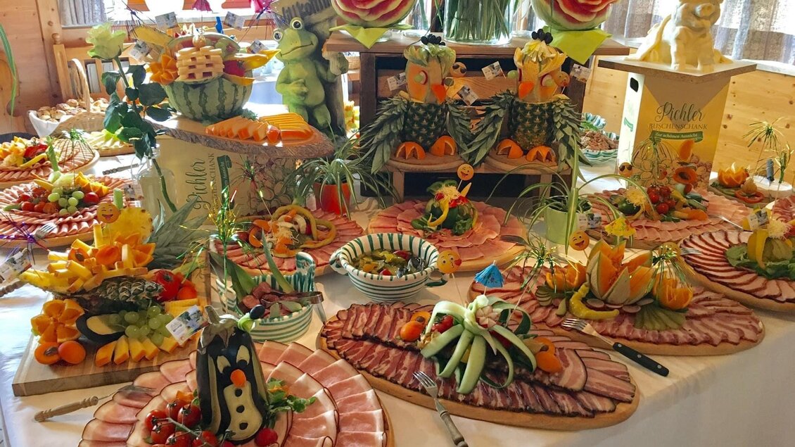 Ein reichhaltiges Büffet mit kunstvoll dekorierten Obst- und Fleischplatten. Die Präsentation zeigt eine Vielzahl an frischen Früchten und Gemüse in kreativen Formen.