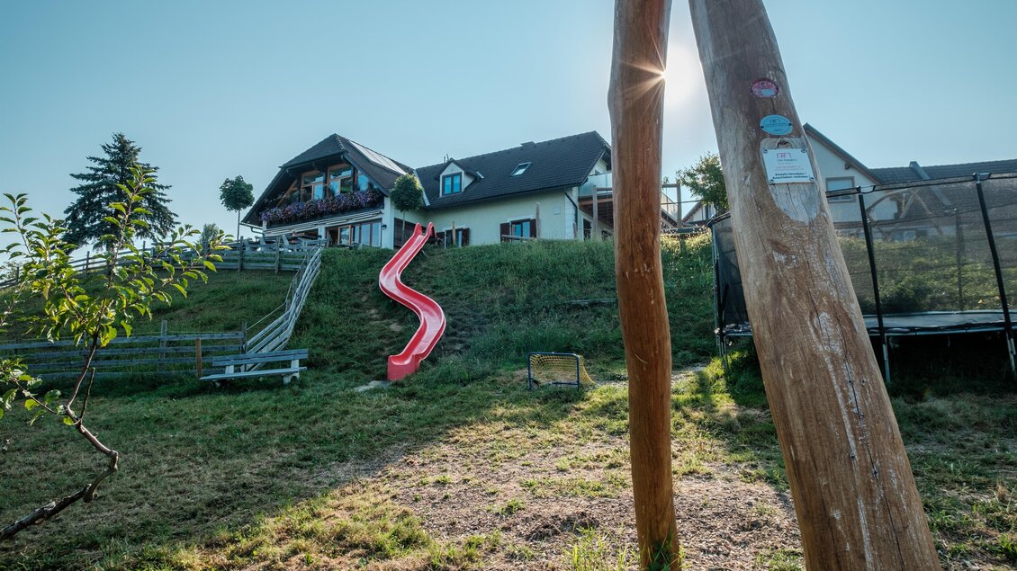Ein Haus mit Rutsche auf einem Hang. Im Hintergrund sind Bäume und ein sonniger Himmel zu sehen. | © MALU