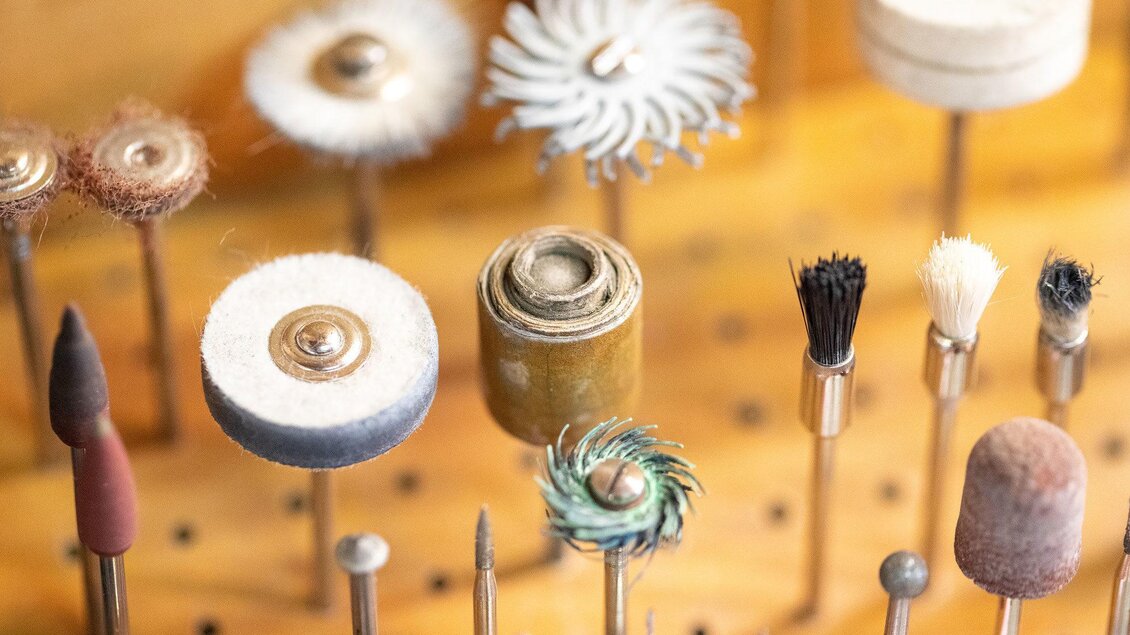 Eine Vielzahl von Werkzeugen und Bürsten für handwerkliche Arbeiten, die auf einem Holzbrett angeordnet sind. Die Werkzeuge sind in verschiedenen Formen und Materialien gehalten. | © Schmuck Design, Marion Buchsteiner