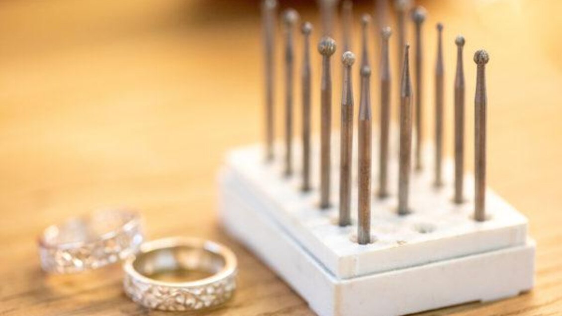 Zwei Ringe liegen neben einem Werkzeughalter mit feinen Stiften. Der Holzuntergrund ergänzt die handwerkliche Atmosphäre. | © Schmuck Design, Marion Buchsteiner