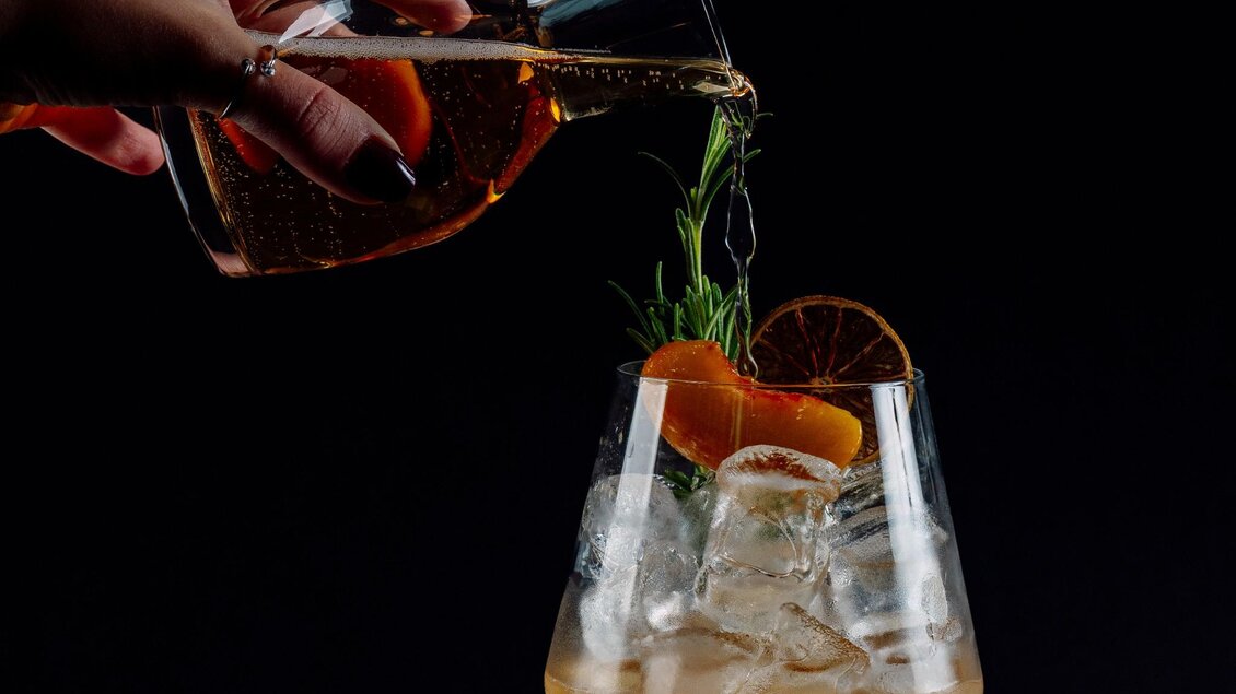 Getränk mit Eis, Rosmarin und Trockenfrucht wird in Glas eingeschenkt. | © MEAT.art - Simona Donko