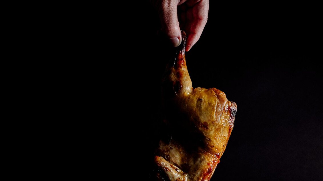 Knusprig gebratenes Hendlstück wird von einer Hand gehalten. | © MEAT.art - Simona Donko