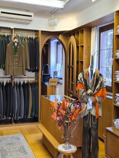 Ein gut sortierter Kleidungsladen mit traditioneller Trachtenmode. An den Wänden hängen verschiedene Anzüge und die Auslage zeigt elegante Accessoires. | © Stephanie Bor