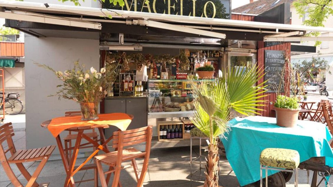 Außenbereich eines Marktstandes in Graz mit Holztischen, Blumenvasen und Palmen im Sonnenschein | © Macello