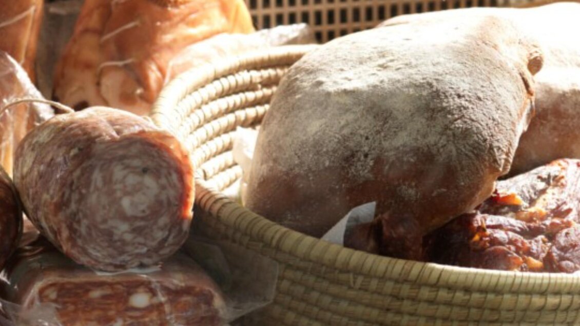 Luftgetrocknete Schinkenkeulen und verschiedene Wurstsorten, präsentiert in einem Korb | © Macello