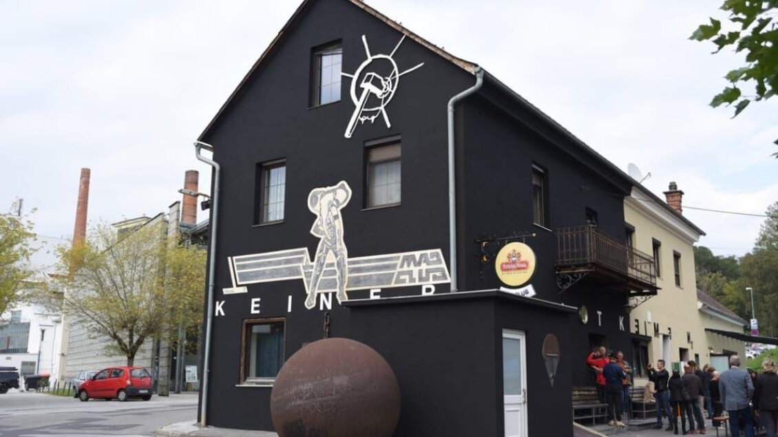 Ein schwarzes Gebäude mit einer auffälligen Wandmalerei. Vor dem Haus steht eine große, runde Skulptur und es sind einige Menschen zu sehen. | © keine Kenntnis