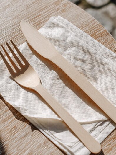 Wooden cutlery consisting of a fork and knife on white napkins on a wooden table. | © Midjourney