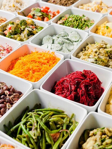 A variety of colorful salads and side dishes in white bowls. The arrangement shows a wide selection of fresh ingredients. | © Mangolds